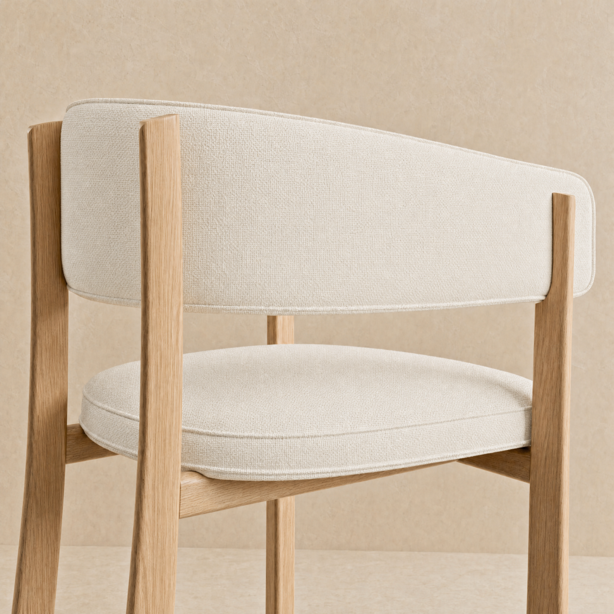 A close-up of a modern dining chair with a light beige textured fabric seat and back cushion, supported by a natural oak wood frame, set against a matching beige textured background.