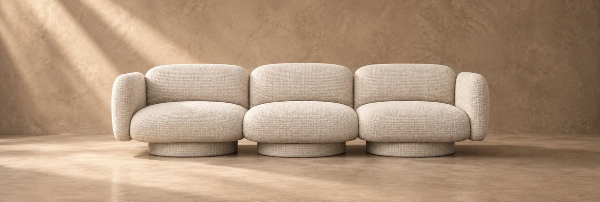Modern beige bouclé modular sofa with curved lines against a textured earth-tone wall.