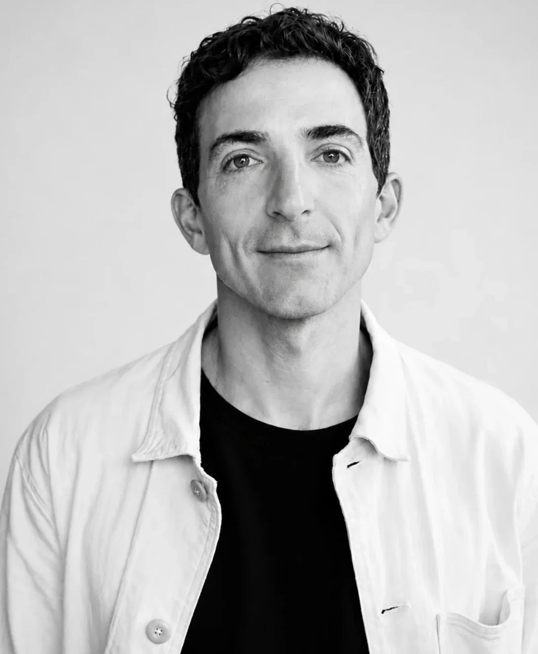 Black and white portrait of a man wearing a white shirt over a black t-shirt.