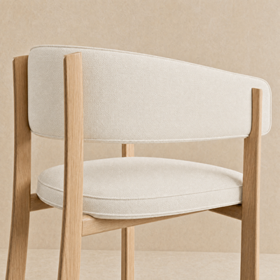 A close-up of a modern dining chair with a light beige textured fabric seat and back cushion, supported by a natural oak wood frame, set against a matching beige textured background.