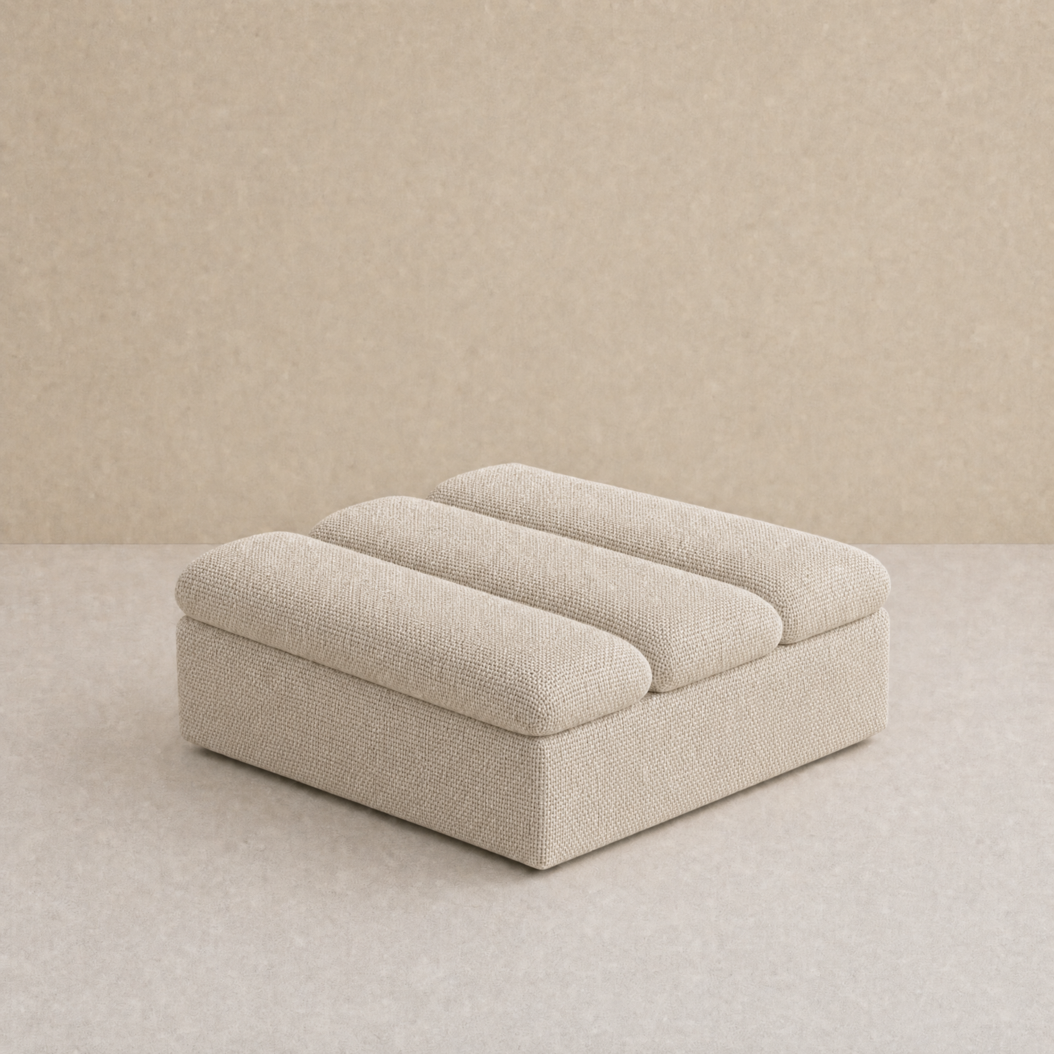 A modern low-profile ottoman or footstool upholstered in a textured beige fabric, featuring three rounded segmented back cushions, set against a matching beige textured studio background.