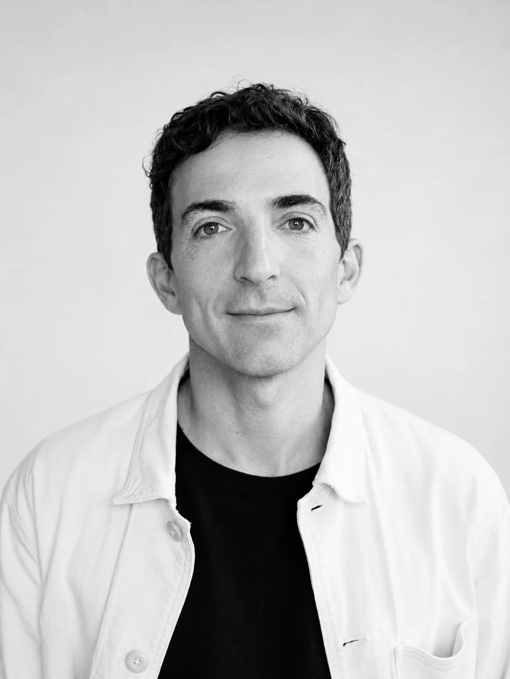 Black and white portrait of a person wearing a light-colored jacket over a dark shirt.