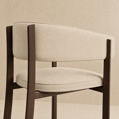 A modern dining chair with a curved backrest and seat cushion upholstered in textured beige fabric, supported by dark brown wooden legs, shown against a neutral beige background.